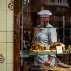 Chef behind a bakery window showcasing gourmet breads on glass shelves.